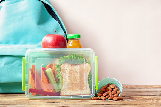 School lunch box with sandwich, vegetables, juice and almonds on table.