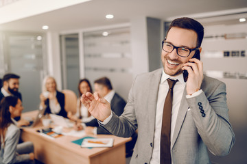 Smiling handsome Caucasian businessman in formal wear standing in boardroom and talking on the...