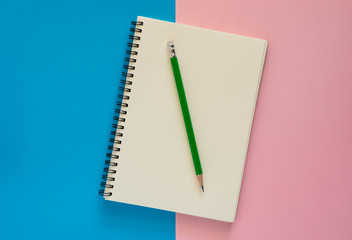 Open notebook with green pencil on pink and blue paper background. - 260050420