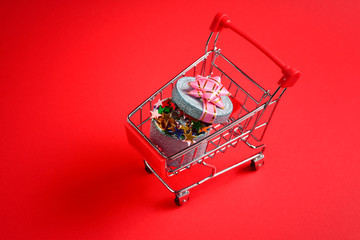 Blue present box with pink bow in a shopping cart on a red background.
