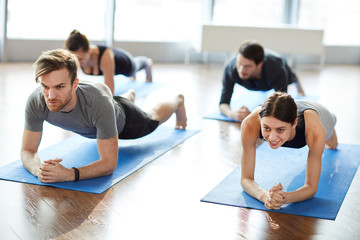 Concentrated motivated young people in sportswear doing elbow plank while strengthening arms and spine at group fitness class - obrazy, fototapety, plakaty