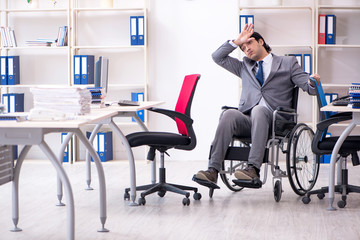 Fototapeta na wymiar Young handsome employee in wheelchair working in the office 