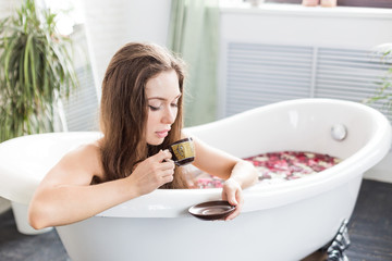 A young attractive girl takes a bathroom with flower petals and relaxes against the background of a beautiful light interior. Spa treatments for beauty and health with skin care
