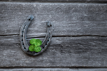 Old horseshoe and four leaf clover on a vintage wooden board. The concept of luck, luck, luck. St. Patricks Day card.