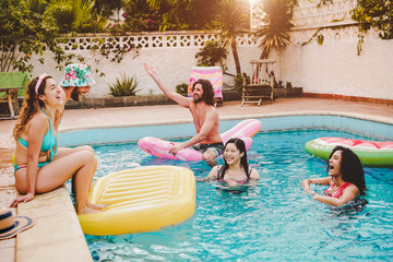 Happy friends having fun in swimming pool  during summer vacation - Young people relaxing and floating on air lilo during in the pool resort - Friendship, holidays and youth lifestyle concept - Powered by Adobe