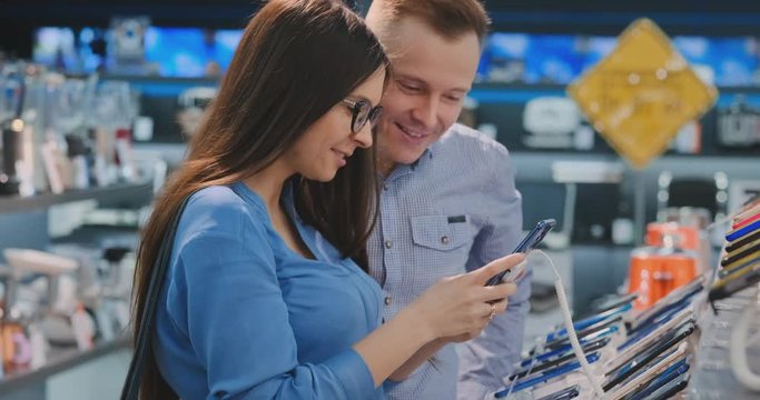 Young beautiful couple. Man and woman hold in hands a smartphone standing near a showcase with smartphones in the appliances store choosing the best smart phone. A gift to his wife