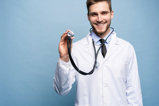 Handsome Young Medic Holding A Stethoscope, Isolated Over Light Blue.