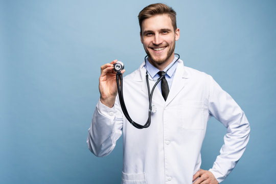Handsome young medic holding a stethoscope, isolated over light blue.