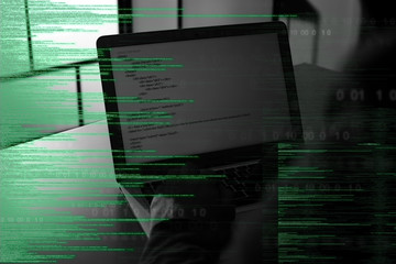 Dark silhouette of cyber criminal hacking computer behind digital symbols, closeup