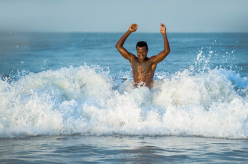 beach portrait of young fit and attractive black African American man with muscular beautiful body enjoying playful in the sea playing on the water having fun