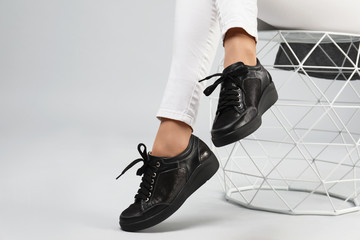 Woman in stylish shoes sitting on stool, grey background. Space for text