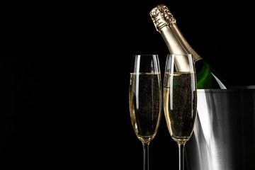 Glasses of champagne near bucket with bottle on black background, space for text