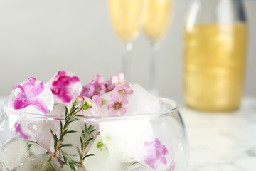 Glass with floral ice cubes on blurred background, closeup. Space for text