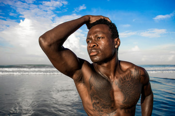 portrait of young attractive and fit black African American man with strong muscular body posing cool model attitude on the beach isolated on Summer blue sky