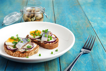 smorrebrod sandwiches with herring boiling egg chopped green onions  on white plate on wooden table 