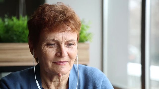 Elderly woman with a wart with a headset and a telephone. Woman pensioner with headphones from the phone and a smartphone in a cafe. Pensioner inserts headphones into her ears. Papilloma warts on the 