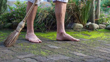 man sweeps paving with a hand made grass broom