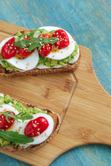 two sandwiches with avocado boiling egg cream cheese cherry tomatoes on cutting board top view