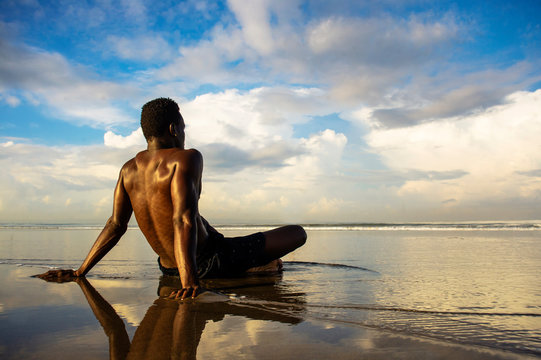 young attractive and relaxed black afro American man with fit body and muscular back sitting on beach sand enjoying beautiful view thinking and meditating free