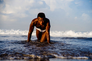 young attractive and sexy black African American man with athletic muscular body posing cool in sea water on desert beach in male beauty and plasticity concept