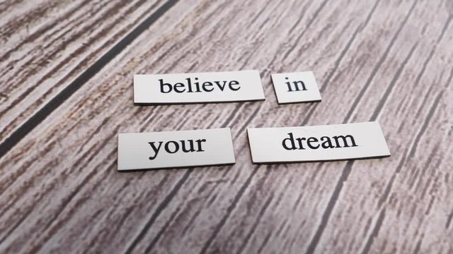 The words BELIEVE IN YOUR DREAM on a table with the camera turning around them.