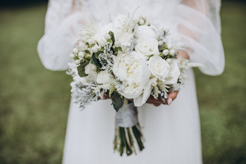 bride in white dress holding a bouquet of white flowers and greenery