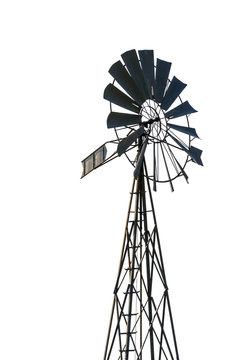 Low angle view of an old-fashioned, multi-bladed, metal wind pump atop a lattice tower in backlight, isolated on white background.