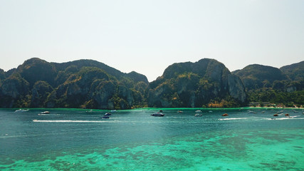 Blue clear water with boats. Green tropical island Phi Phi, palm trees grow. Shooting from a drone from the air. Beautiful seascape. Turquoise color of the water, you can see the bottom and corals.