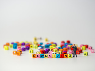 miniature figure businessman in dark blue suit standing backside of colorful of downsizing alphabet and thinking abount how to Reduce trade, spend and downsizing Organization.