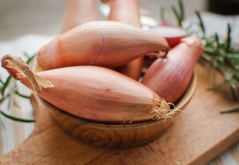 Close-up of shallots in a wooden bowl with fresh rosemary on cutting board - obrazy, fototapety, plakaty