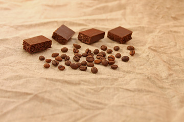 Chocolate cubes with coffee beans on a linen texture background.
