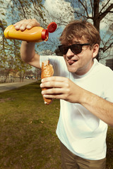 Man in street park eating hot dog with mustard, ketchup and dough bun