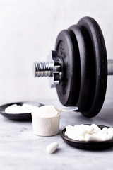 Scoop of Whey Protein, Creatine, Taurine capsules and a dumbbell. Bodybuilding food supplements on stone / wooden background. Close up. Copy space.