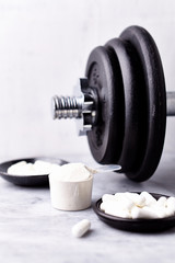 Obraz na płótnie Canvas Scoop of Whey Protein, Creatine, Taurine capsules and a dumbbell. Bodybuilding food supplements on stone / wooden background. Close up. Copy space.