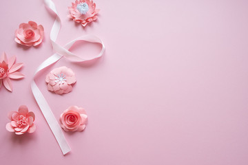 frame with pink paper flowers and pink ribbon on pink background.