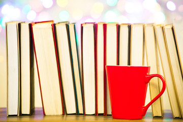 A red mug with a heart, against a background of a row of books and bokeh lights