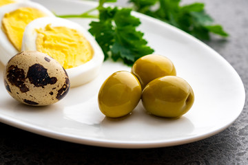Boiled chicken eggs with quail eggs, olive and parsley on the white plate