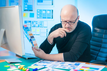 A creative man is developing a graphic design for a mobile application. The work of the designer. A middle aged man works at a computer. Selection of colors for web design.