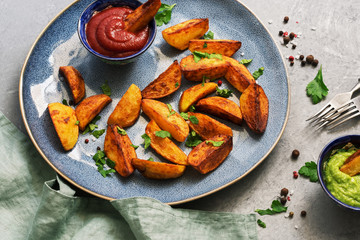 Fried potatoes with tomato sauce and guacamole in a plate on a gray background. Selective focus