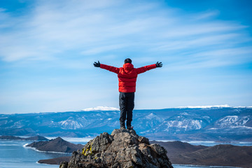 Traveler man wear red clothes and raising arm standing on mountain at daytime in Lake Baikal, Siberia, Russia.