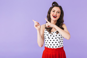 Portrait of cheery pin-up woman 20s in vintage polka dot dress pointing fingers aside at copyspace