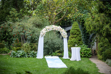 Fototapeta premium Beautiful wedding ceremony outdoors. Decorated chairs stand on the grass. Wedding arch made of cloth and white and pink flowers on a green natural background.