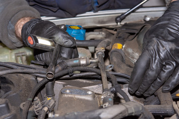 Fototapeta na wymiar Car mechanic repairs diesel engine. Old and dirty car engine with car mechanics hands. Car repairing concept in the garage workshop.