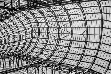 Through the glass covered steel roof, a black and white look up at a London shopping gallery  area.