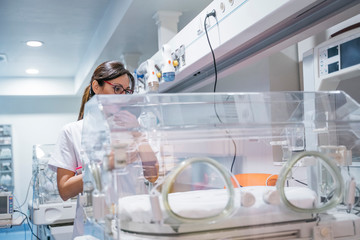 Female doctor examining newborn baby in incubator - obrazy, fototapety, plakaty