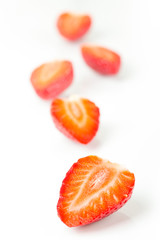 Red fresh strawberries cut into half arranged on a white background.