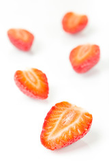 Red fresh strawberries cut into half arranged on a white background