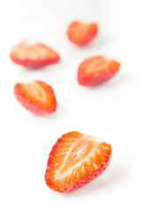 Red fresh strawberries cut into half arranged on a white background