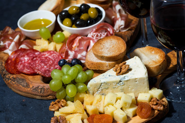 cheese platter on a wooden board, bread, fruit and cold cuts, closeup