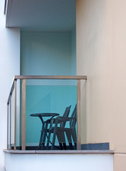 a balcony in a white modern concrete building with steel railings and a glass surround with black plastic chars and a table